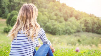 Girl sitting on a green meadow and watching the countryside landscape.