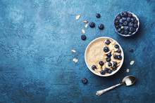 Bowl Of Oatmeal Porridge With Banana And Blueberry On Vintage Table Top View In Flat Lay Style. Healthy Breakfast And Diet Food.