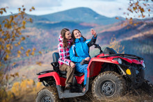 Happy Female Riders In Jackets On Red Quad Bike At The Hill Makes Selfie On The Phone With Mountains In Blurred Background. Sunny Autumn Day