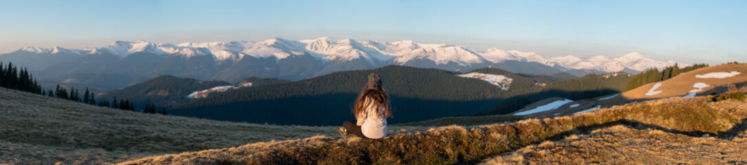 panoramic rearview shot of a female enjoying gorgeous view in the early morning sitting on top of a 