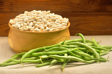 A bowl with raw beans among green bean on a wooden background