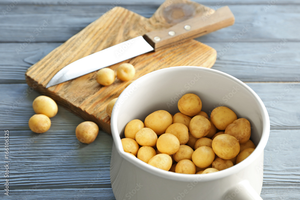 Saucepan with raw organic potato on wooden table