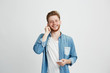 © Cookie Studio - Young cheerful guy in headphones smiling holding phone looking at camera listening to music over white background.