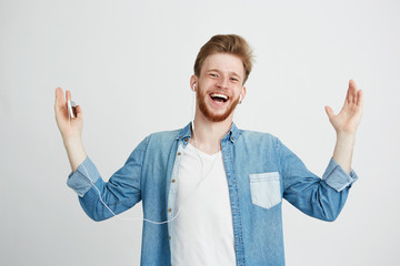 Wall Mural - Happy young man smiling listening to streaming music in headphones singing looking at camera over white background.