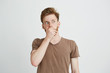 © Cookie Studio - Portrait of surprised frightened scared young man looking in side closing mouth with hands over white background.