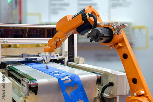 Fotografiet Robot gripping a workpiece out of the machine via a conveyor belt for smart factory, industry 4