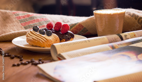 Cappuccino, cake with berries and a journa on table. Tableau sur Toile