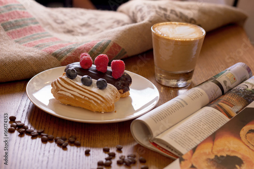 Cappuccino, cake with berries and a journa on table. Tableau sur Toile