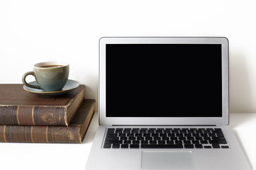 Cropped shot of open laptop computer, two books and mug of coffee or tea resting on white desk. Technology, communication, job, occupation and leisure concept. Freelancer's workplace. Mock up