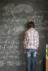 Teenageer Boy, standing near blackboard and having trouble with complicated math formulas