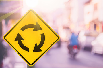 Wall Mural - Roundabout warning sign on blur traffic road with colorful bokeh light abstract background.