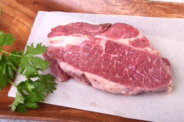 Raw beef steak with spices Leaves of coriander on wooden cutting board. Ready for cooking.