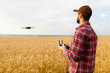 © artiemedvedev - Farmer holds remote controller with his hands while copter is flying on background. Drone hovers behind the agronomist in wheat field. Agricultural new technologies and innovations. Back view