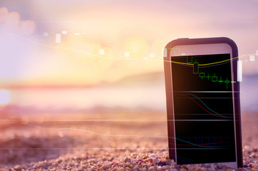 Business economic technology and freedom trader working concept. Close up smart phone on sand sunset beach double expose with graph money stock currency background.