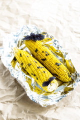 Two corn cobs baked in foil with basil