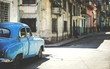© Mint Images - Classic 1950s car parked on street of dilapidated buildings
