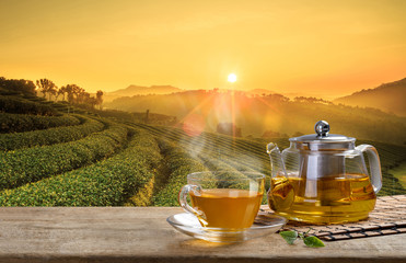 Wall Mural - Tea cup and glass jugs or jars. with and tea leaf sacking on the wooden table and the tea plantations background