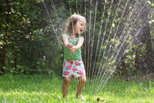 Happy Toddler Girl Playing In A Sprinkler On A Hot Summer Day