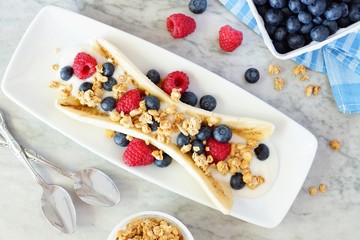 Wall Mural - Healthy banana split with yogurt, fresh berries and granola, overhead scene on marble