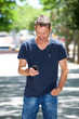 © mimagephotos - Happy man standing outside with cellphone laughing on sidewalk