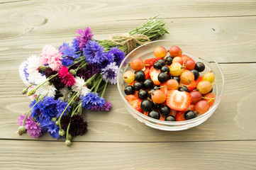 Wall Mural - bowl full of fresh berries on the wooden background with flower cornflowers