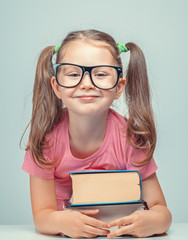Wall Mural - smiling beautiful cute little girl leaning on thick books while looking at camera