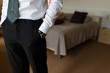 © korchemkin - Businessman in white shirt holding hands with watches in the pockets of black trousers in an hotel room before an important meeting. Serious handsome man in casual white shirt, black tie, black pants.