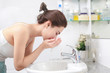 Woman washing her face with water above bathroom sink.