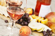 Two glasses of rose wine and board with fruits, bread and cheese on wooden table