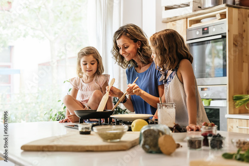 Photographie Little sisters cooking with her mother in the kitchen.