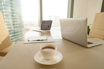 Modern office workplace with conference negotiating table and two laptops, focus on cup of coffee, break during work, preparation to formal meeting in boardroom, executive management working space