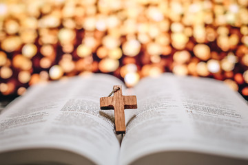 Closeup of the wooden cross on open holy bible with bokeh lighting background