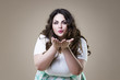 Plus size fashion model sends air kiss, fat woman on beige background, overweight female body