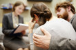 © pressmaster - Back view image of young woman crying in couples counseling session with  husband hugging her supportively
