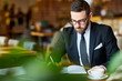 © pressmaster - Elegant trader sitting in cafe and making notes in notebook