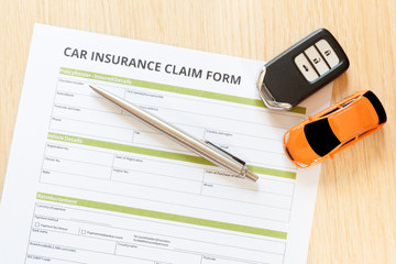 Wall Mural - Top view of car insurance claim form with car toy and car key on wooden desk.