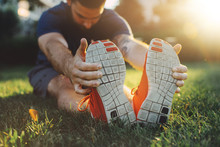 Attractive Young Man Stretching In The Park Before Running At The Sunset Focus On Shoes