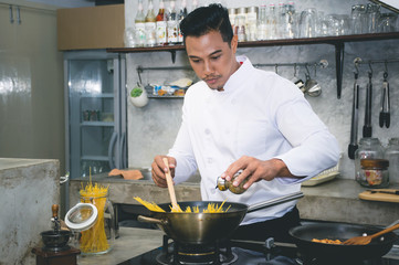 Asian chef is cooking food by using wooden ladle at the kitchen of a restaurant