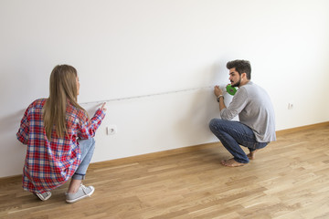 Young couple in empty flat measure wall