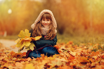 autumn outdoor portrait of beautiful happy child girl walking in park or forest in warm knitted scarf