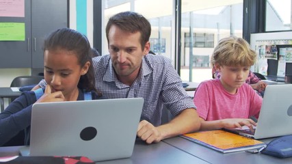 Wall Mural - Teacher helping young students using laptops in class