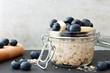 Jar of overnight oats with fresh blueberries and bananas, scene with white and black stone background