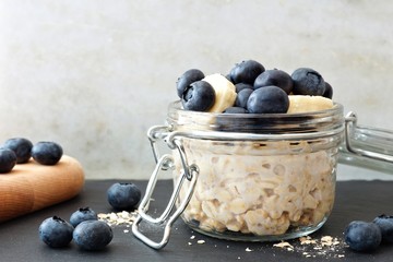 jar of overnight oats with fresh blueberries and bananas, scene with white and black stone backgroun