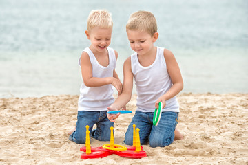 Two brothers are walking and playing on the beach.The game is a ring toss.