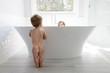 © Jakob/Stocksy - Naked toddler looking at her sister in a big bathtub