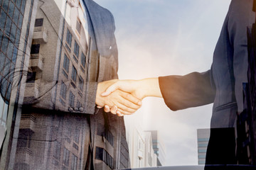 Handshake of business partners on office building background - Double exposure photo