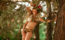 Beautiful Little Girl In Image Of Nymph Dryad Stands Near Tree In Magical Forest .