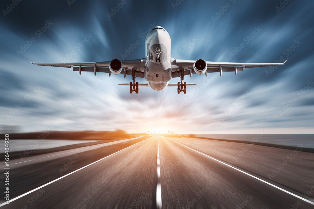 Airplane and road with motion blur effect at sunset. Landscape with passenger airplane is flying over the asphalt road and cloudy sky. Commercial plane is landing. Aircraft with blurred background  - obrazy, fototapety, plakaty 