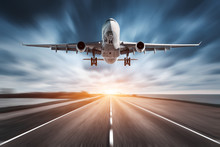 Airplane And Road With Motion Blur Effect At Sunset. Landscape With Passenger Airplane Is Flying Over The Asphalt Road And Cloudy Sky. Commercial Plane Is Landing. Aircraft With Blurred Background 