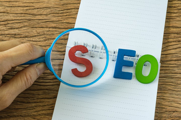 Aufkleber - hand holding magnifying glass on colorful alphabets abbreviation seo on white note paper on the wood